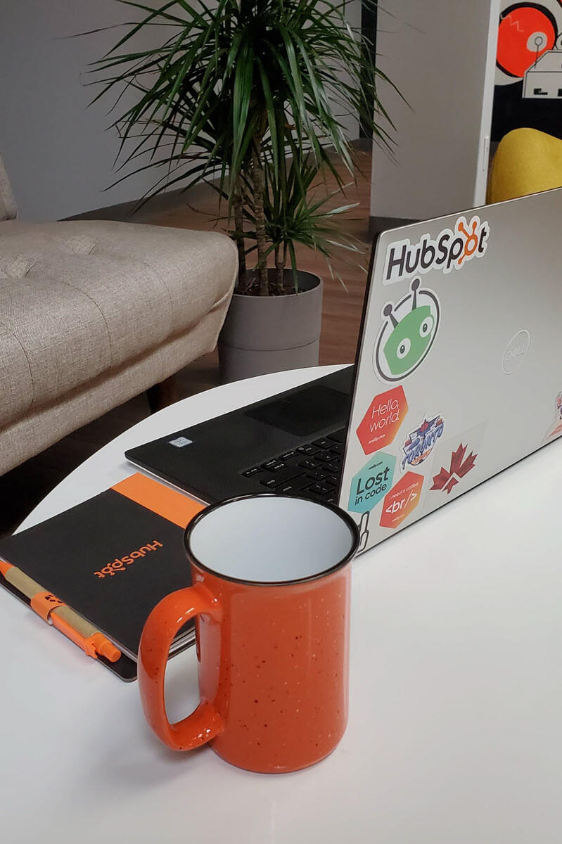 Table with a laptop with HubSpot stickers, a HubSpot notebook and a HubSpot Community Champion mug